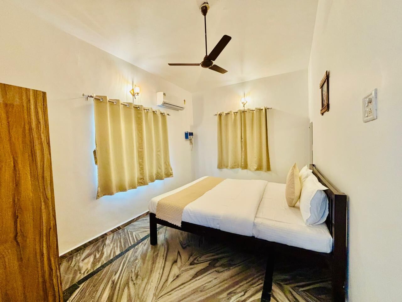 A bedroom with a bed, curtains, a ceiling fan, and an air conditioning unit.