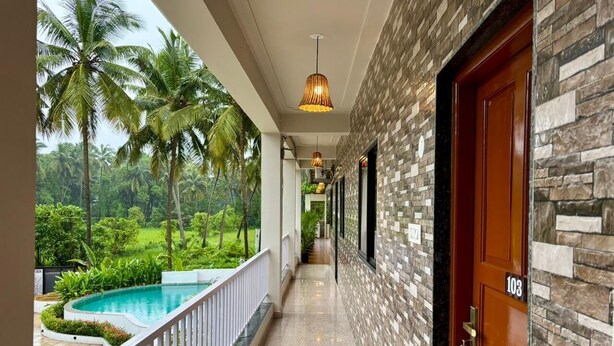 A corridor with a pool, palm trees, and a stone wall. - Zuna Stayz Morjim Goa (Morjim)