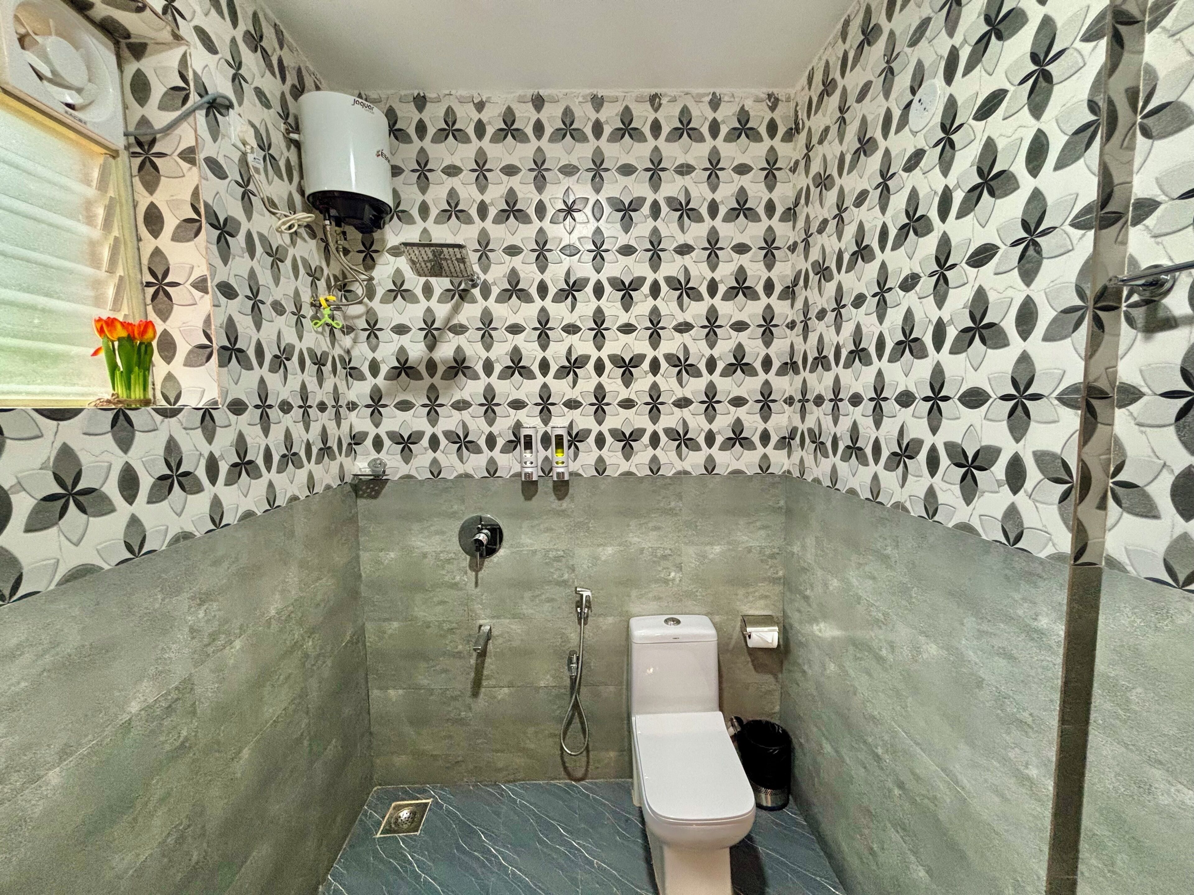 A bathroom with a toilet, shower, and a small window with a vase of flowers.