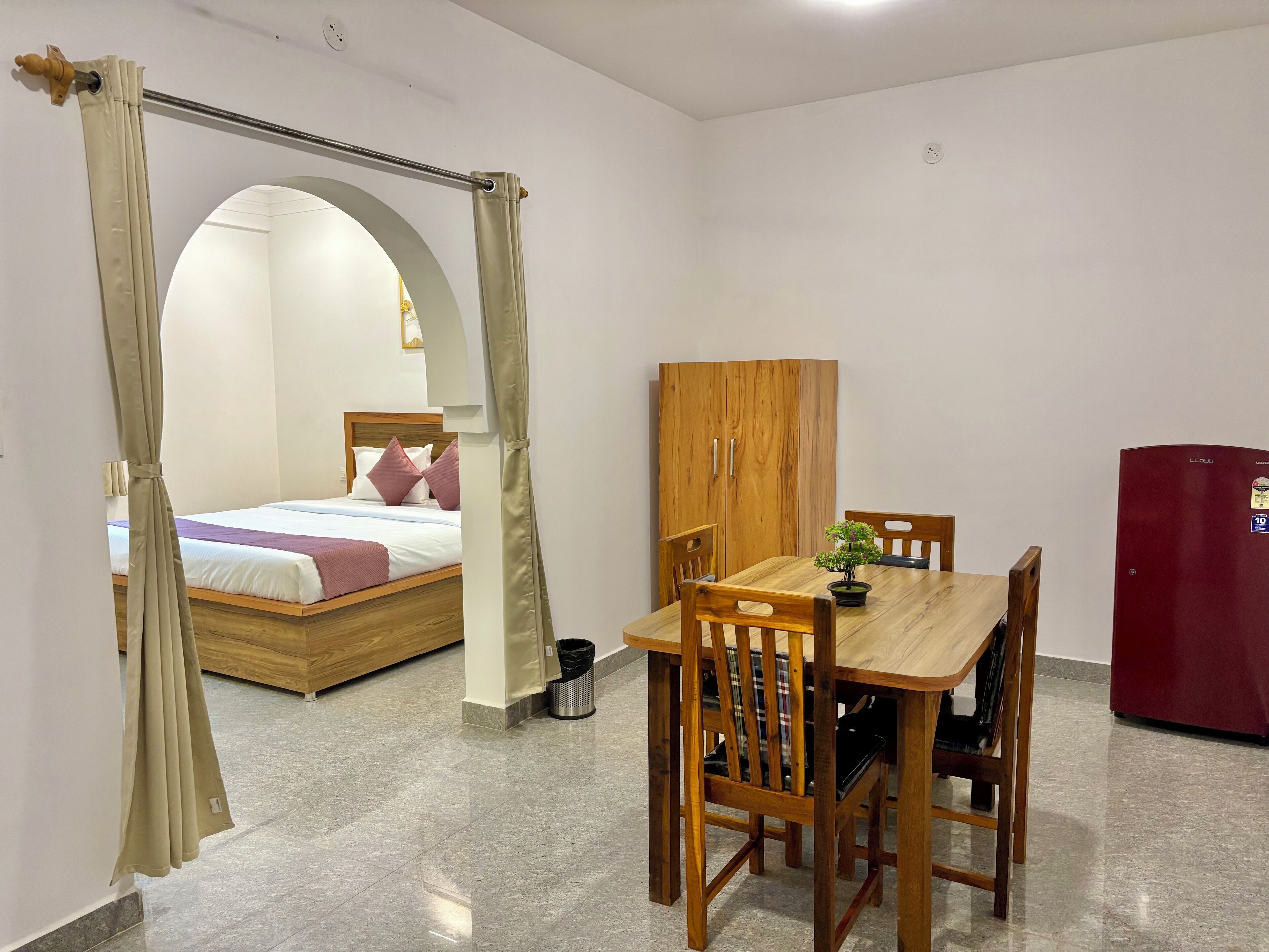 Una habitación con una cama, una mesa de madera con sillas, un armario de madera y un refrigerador rojo.