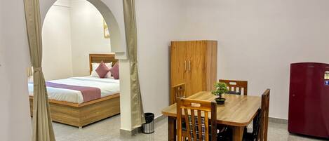 A room with a bed, a wooden table with chairs, a wooden wardrobe, and a red refrigerator.