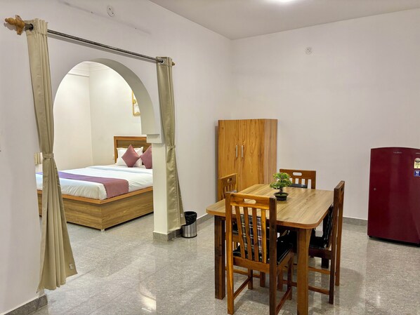 A room with a bed, a wooden table with chairs, a wooden wardrobe, and a red refrigerator.