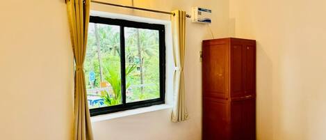 A room with a bed, a window with curtains, a wooden wardrobe, and an air conditioning unit.