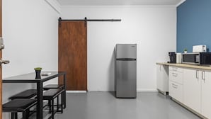 Eine kompakte Küche mit einem Edelstahlkühlschrank, einer Holztür und einem weißen Küchenschrank mit einer Mikrowelle.