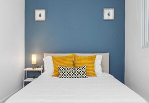 A bed with white bedding, two yellow patterned pillows, and a checkered pillow. - Tranquil | A Mere 4-Minute Saunter to the coast (San Juan)