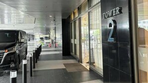 Ein moderner Gebäudeeingang mit schwarzem Fassadenschmuck, einem Schild mit der Aufschrift "TOWER 2" und einem Parkplatz mit einem schwarzen SUV.