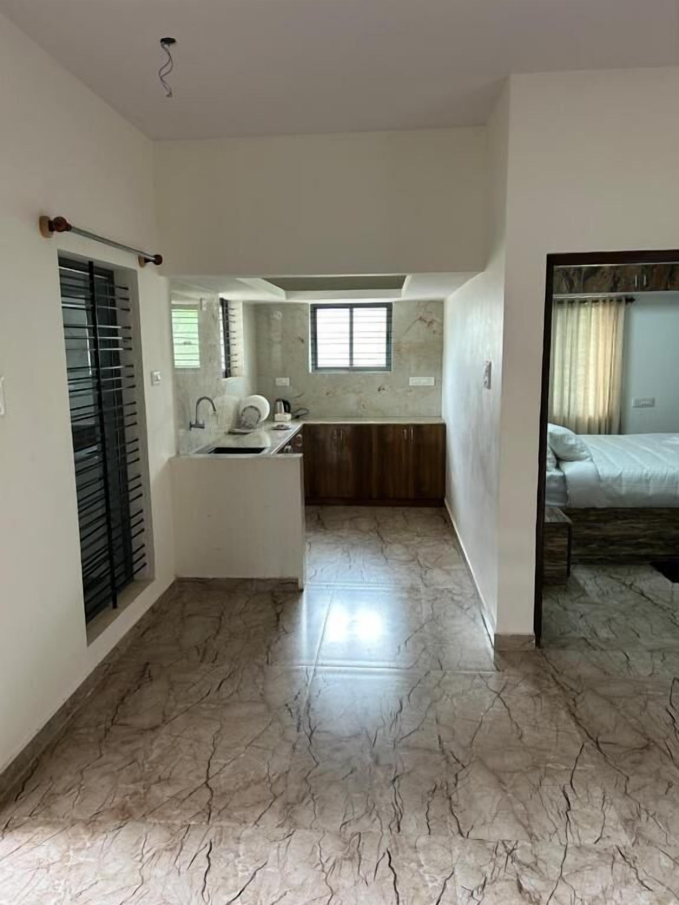 A spacious room with a marble floor, a small kitchenette, a bed with a canopy, and a window with curtains.