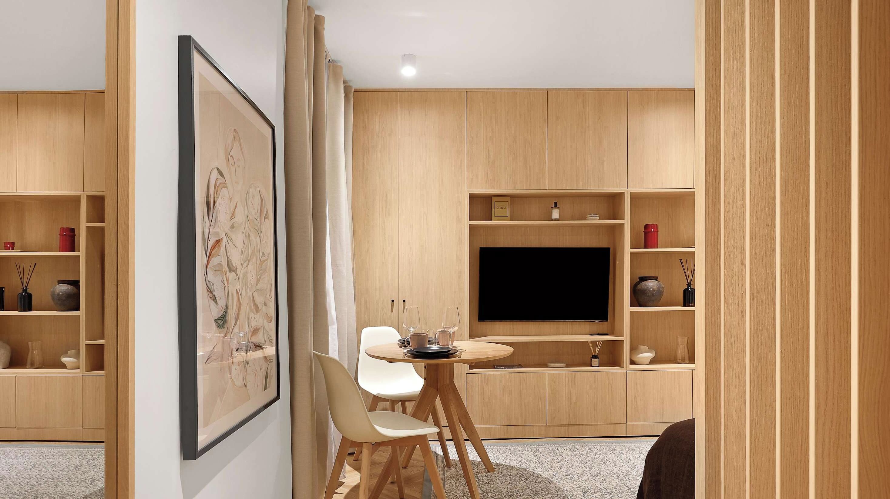 Un soggiorno moderno con una televisione a schermo piatto, mobili contenitori in legno, un tavolo da pranzo con sedie e un'opera d'arte incorniciata appesa al muro.