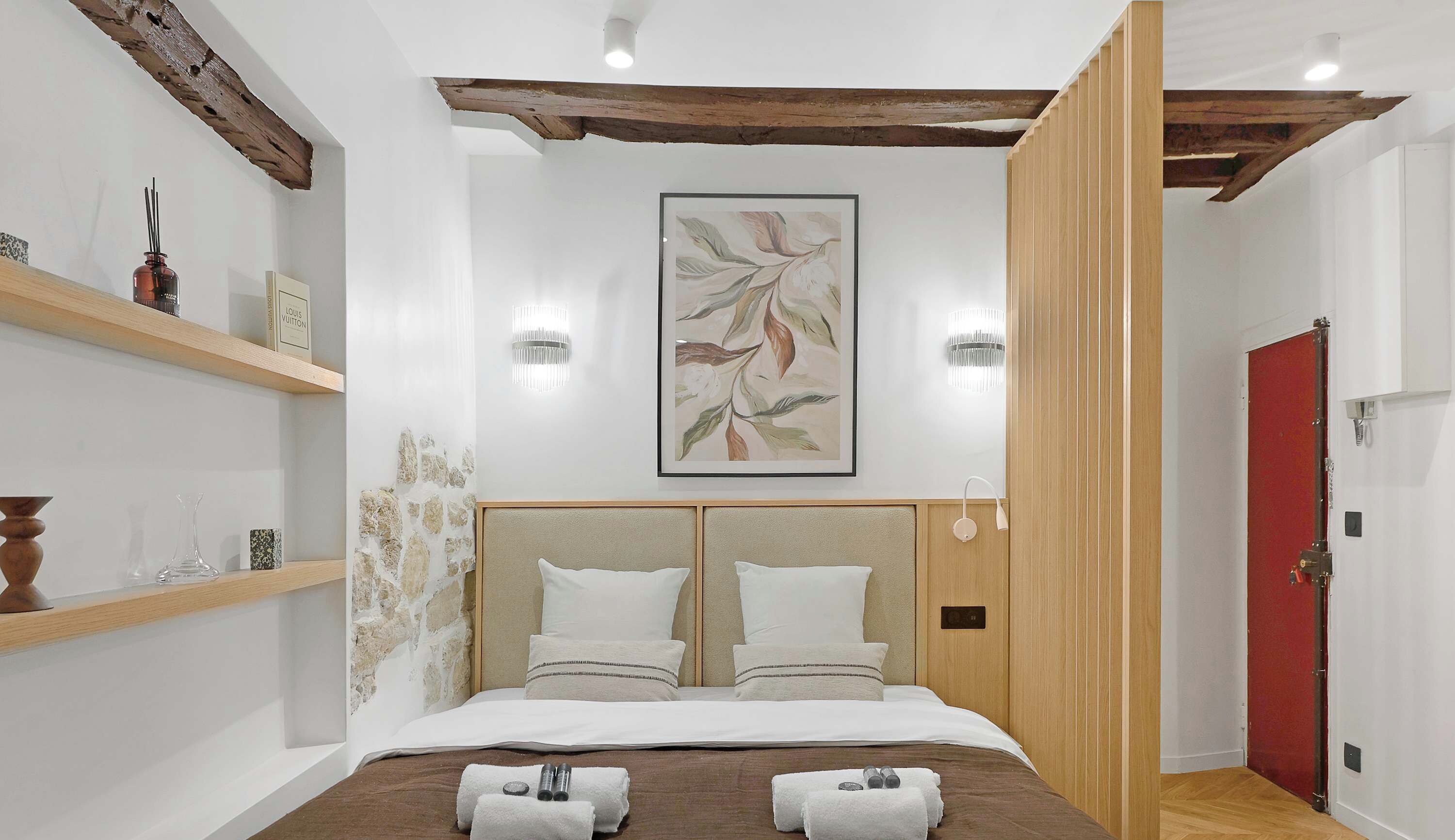 A modern hotel room with a large bed, wooden headboard, and a red door.