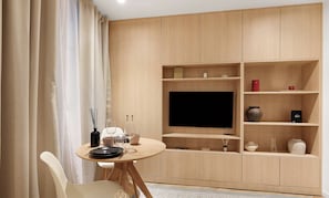Una sala de estar moderna con una mesa redonda de madera, sillas blancas, un televisor de pantalla plana y estantes empotrados de madera con objetos decorativos.