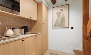 Cocina moderna con armarios de madera, microondas, tetera y tostadora. Hay una obra de arte enmarcada en la pared y suelo de madera.