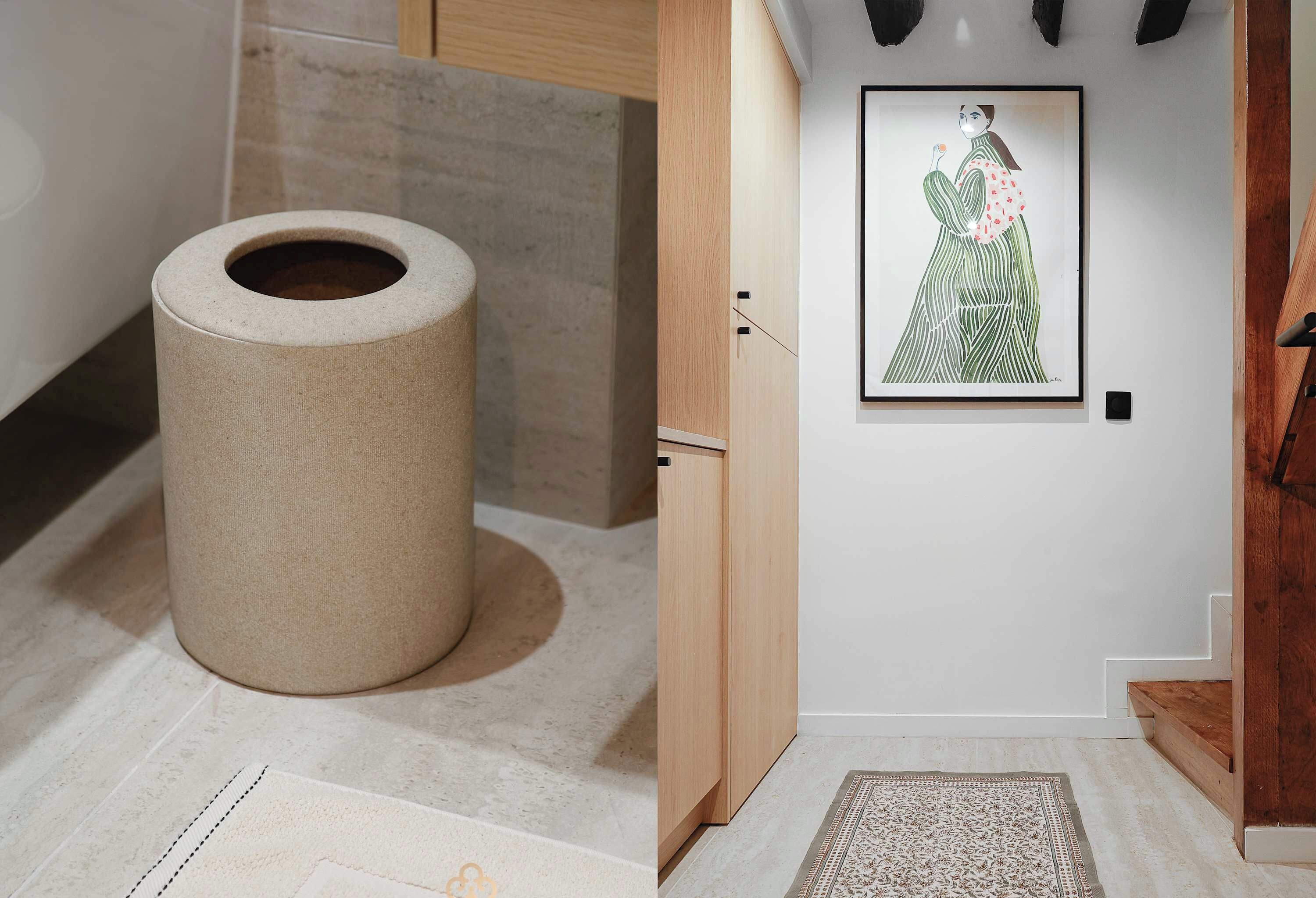 A modern interior with a large, cylindrical object on the floor, a wooden cabinet, a framed artwork on the wall, and a patterned rug.