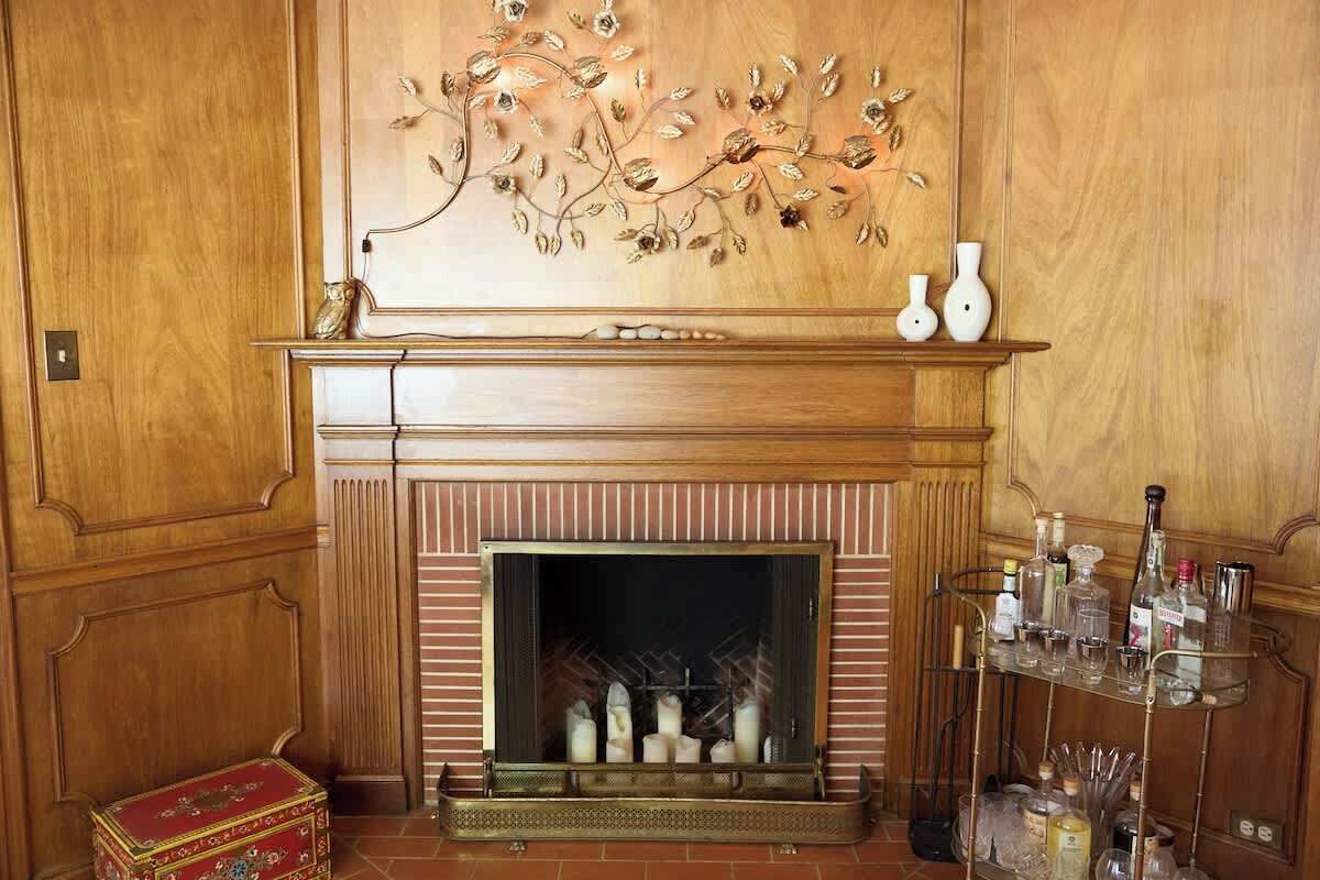 Una chimenea con detalles decorativos, un estante con jarrones y una vitrina de vidrio con botellas.