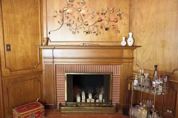 Una chimenea con detalles decorativos, un estante con jarrones y una vitrina de vidrio con botellas.