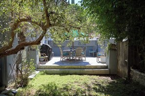 Un patio al aire libre con una mesa y sillas, rodeado por una cerca y follaje.