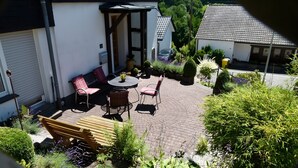 Eine Terrasse mit Gartenmöbeln, ein Garten mit verschiedenen Pflanzen und ein Gebäude mit einem Ziegeldach.