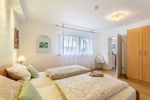 Habitación de hotel con dos camas, un armario de madera, una mesita, una silla y una ventana con cortinas.