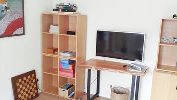 Una habitación con piso de madera, televisor sobre un mueble, una estantería y un cuadro en la pared.