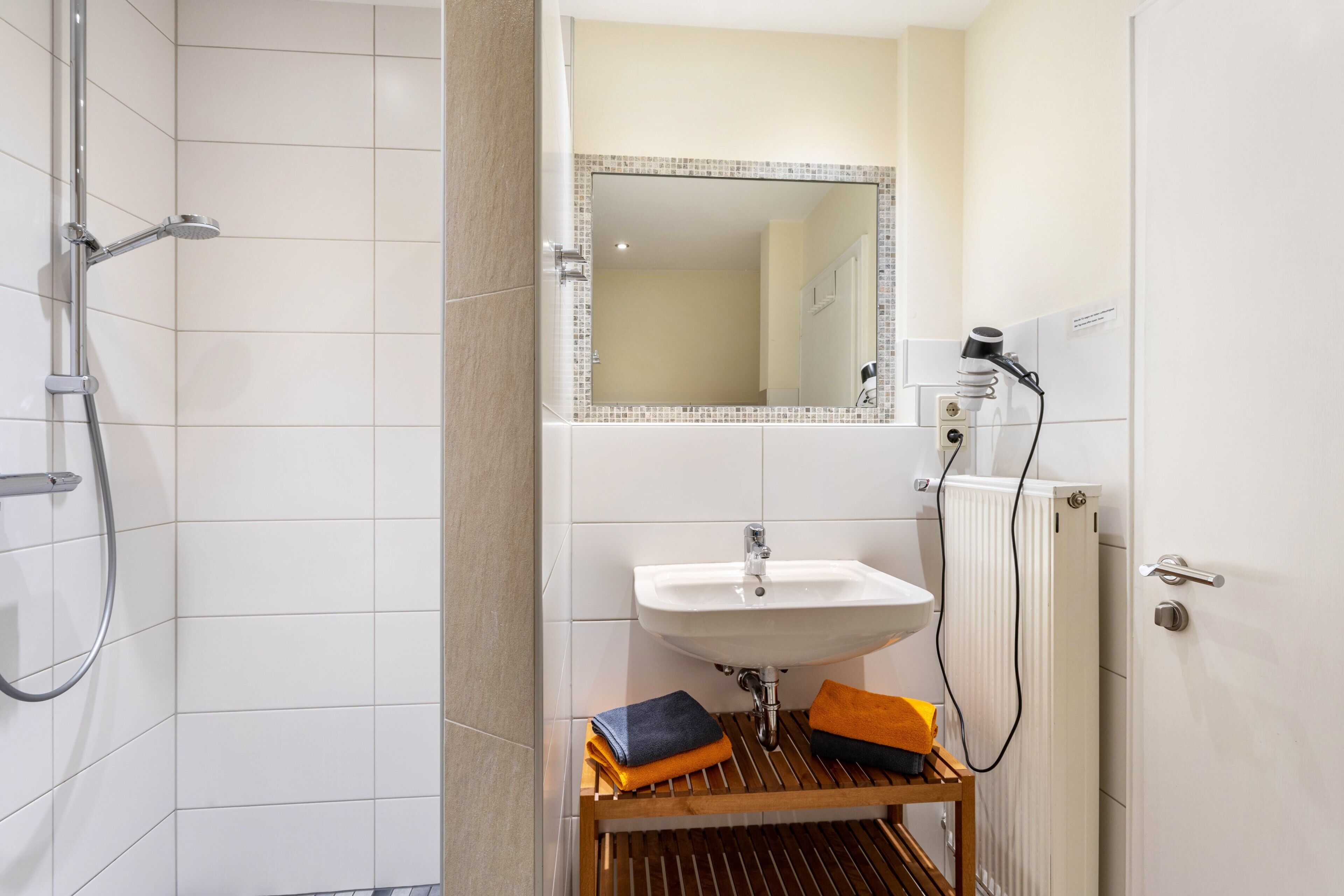 A bathroom with a shower, sink, mirror, and towel rack.