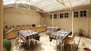 A covered dining area with tables set for meals, a buffet line, and a potted plant. - Harmony Sentiments-The Mall Road (Shimla)