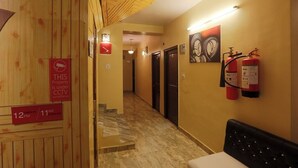 A hotel hallway with a check-out sign, CCTV surveillance notice, fire extinguishers, and a bench. - Harmony Sentiments-The Mall Road (Shimla)