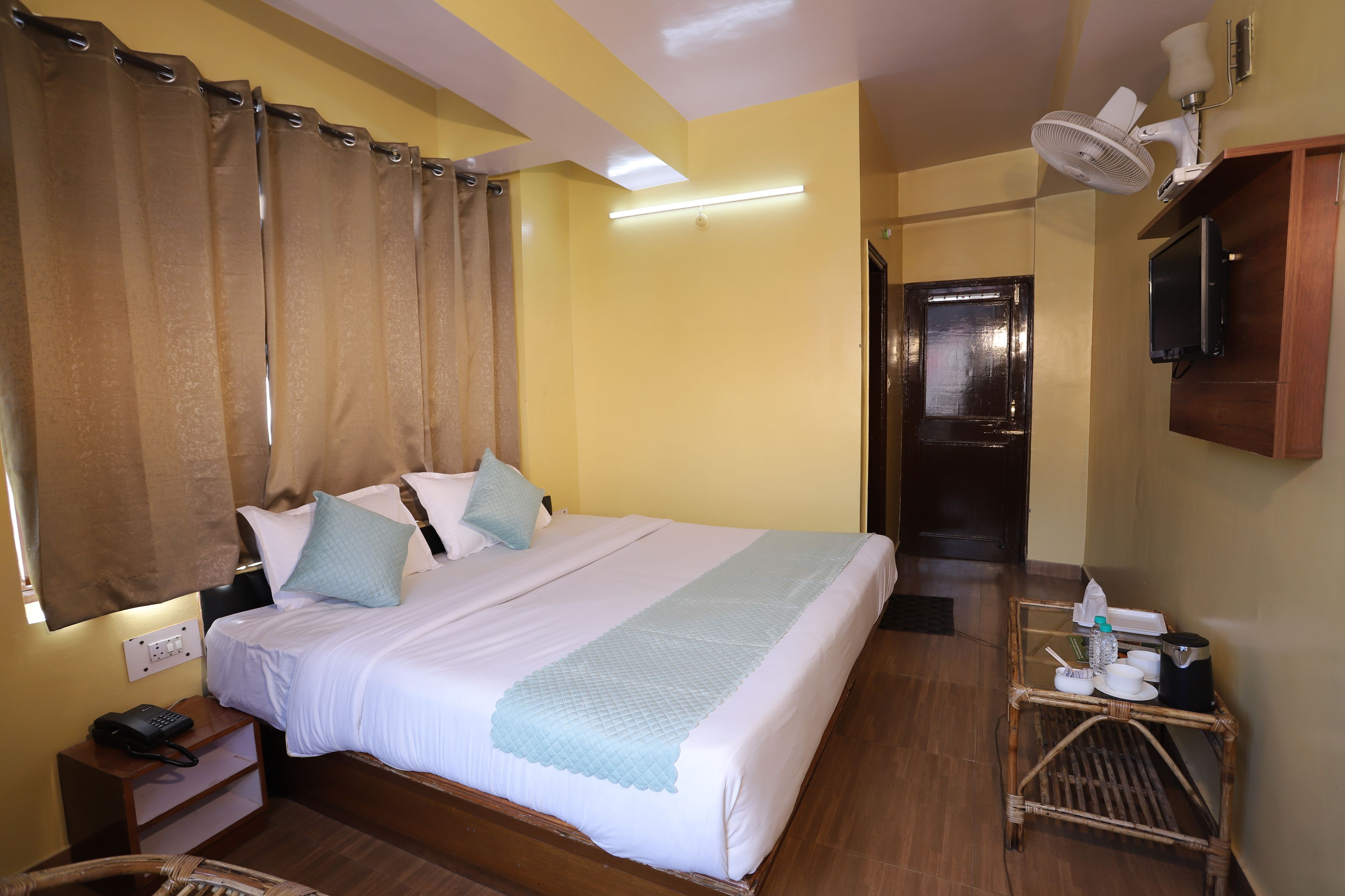 A hotel room with a bed, bedside table, lamp, and a small table with a bottle and glasses.