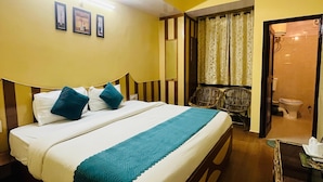 A hotel room with a bed, a small table, a chair, a bathroom visible through an open door, and framed pictures on the wall. - Harmony Sentiments-The Mall Road (Shimla)