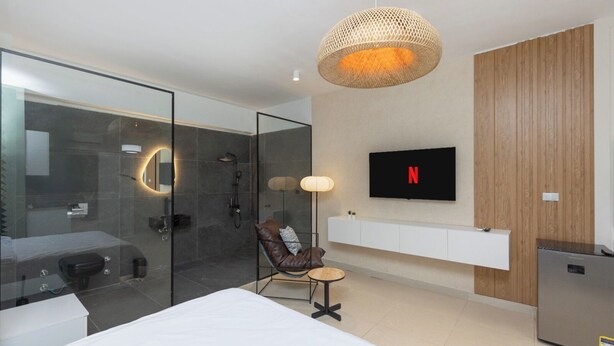 Un dormitorio moderno con cabina de ducha de vidrio, una cama, un televisor montado y un panel de pared de madera.