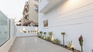 Un edificio moderno con fachada blanca y limpia, un patio empedrado y pequeñas macetas a lo largo de la pared.
