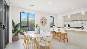 A modern kitchen with white cabinetry, a central island, and pendant lighting. - Serendipity Shell Cove (Shell Cove)