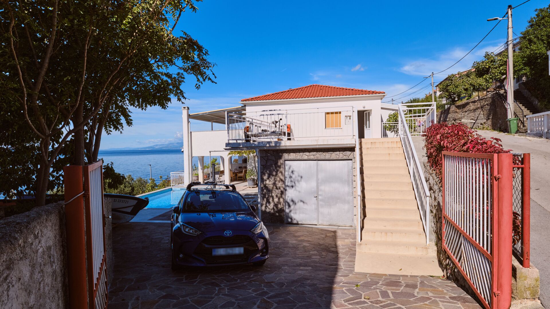 A coastal property with a car parked in front, a stone staircase, and a view of the sea.