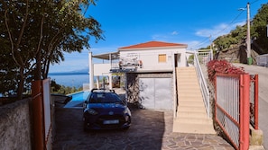 Une propriété située sur la côte, avec une voiture garée devant, un escalier en pierre et une vue sur la mer.
