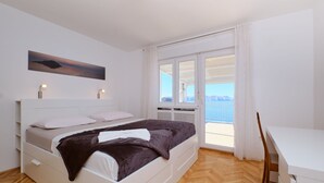 Un dormitorio con cama, lámparas de noche, un cuadro, una ventana con vistas y un balcón.
