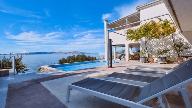 Zona junto a la piscina con sillones, piscina y vista al mar y a las montañas.