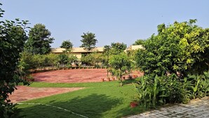 A courtyard with a paved area, surrounded by greenery and trees. - JHAR ARRAVLI RESORT  (Bassi)