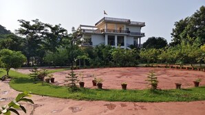 A modern building with a balcony, surrounded by a landscaped garden with potted plants and a grassy area. - JHAR ARRAVLI RESORT  (Bassi)