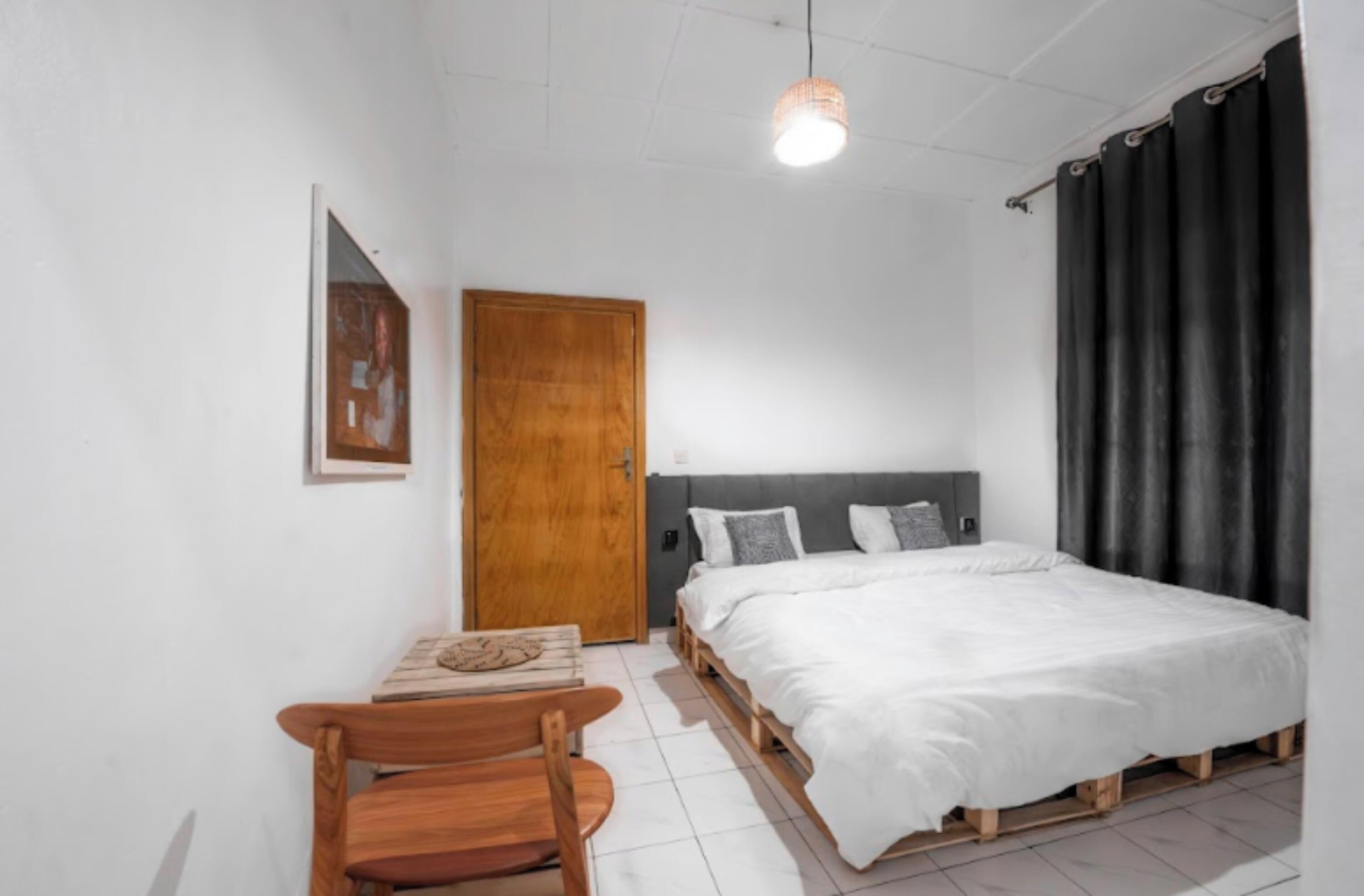 Un dormitorio con cama, una puerta de madera, una mesita con silla y una lámpara colgante.