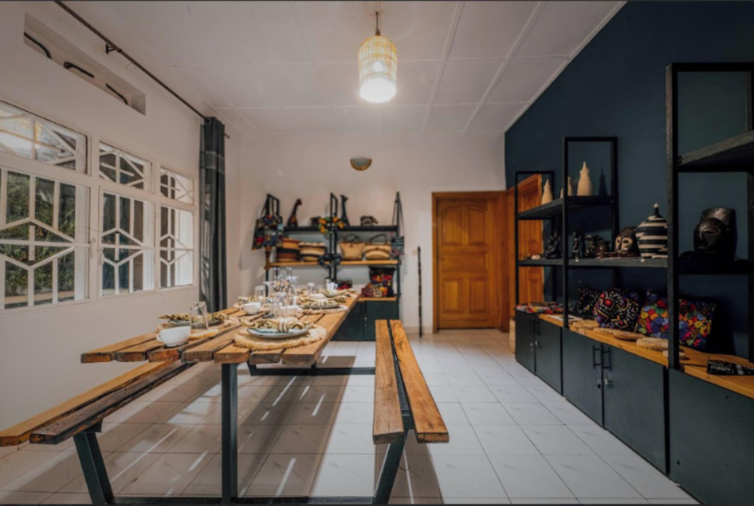 A kitchen with a long wooden table set for a meal, shelves with kitchenware, and a hanging light fixture.