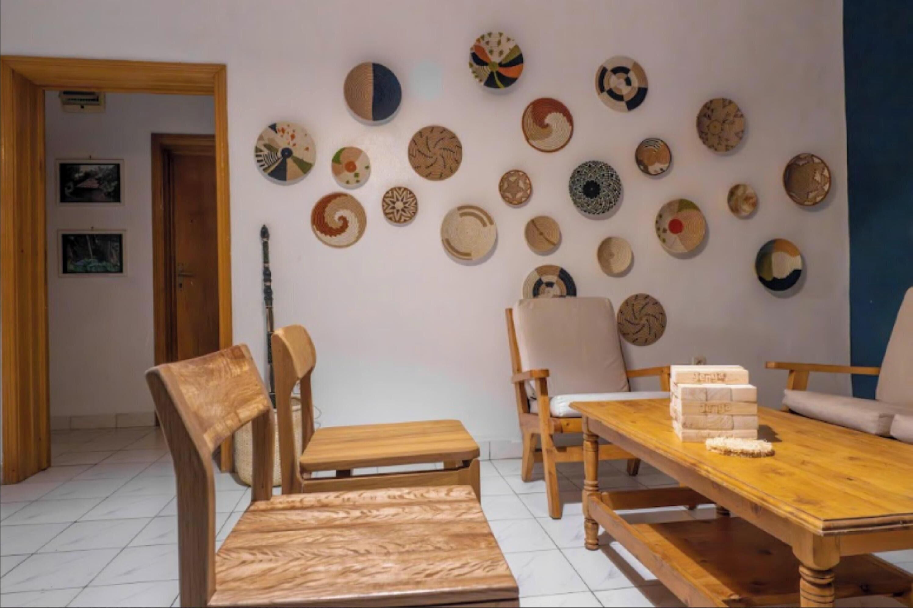 Un comedor con una mesa y sillas de madera, una pared decorada con distintos platos, y una puerta que da a otra habitación.