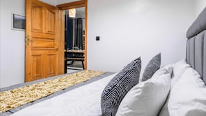 Un dormitorio con una cama, almohadas, una puerta de madera y una alfombra estampada.
