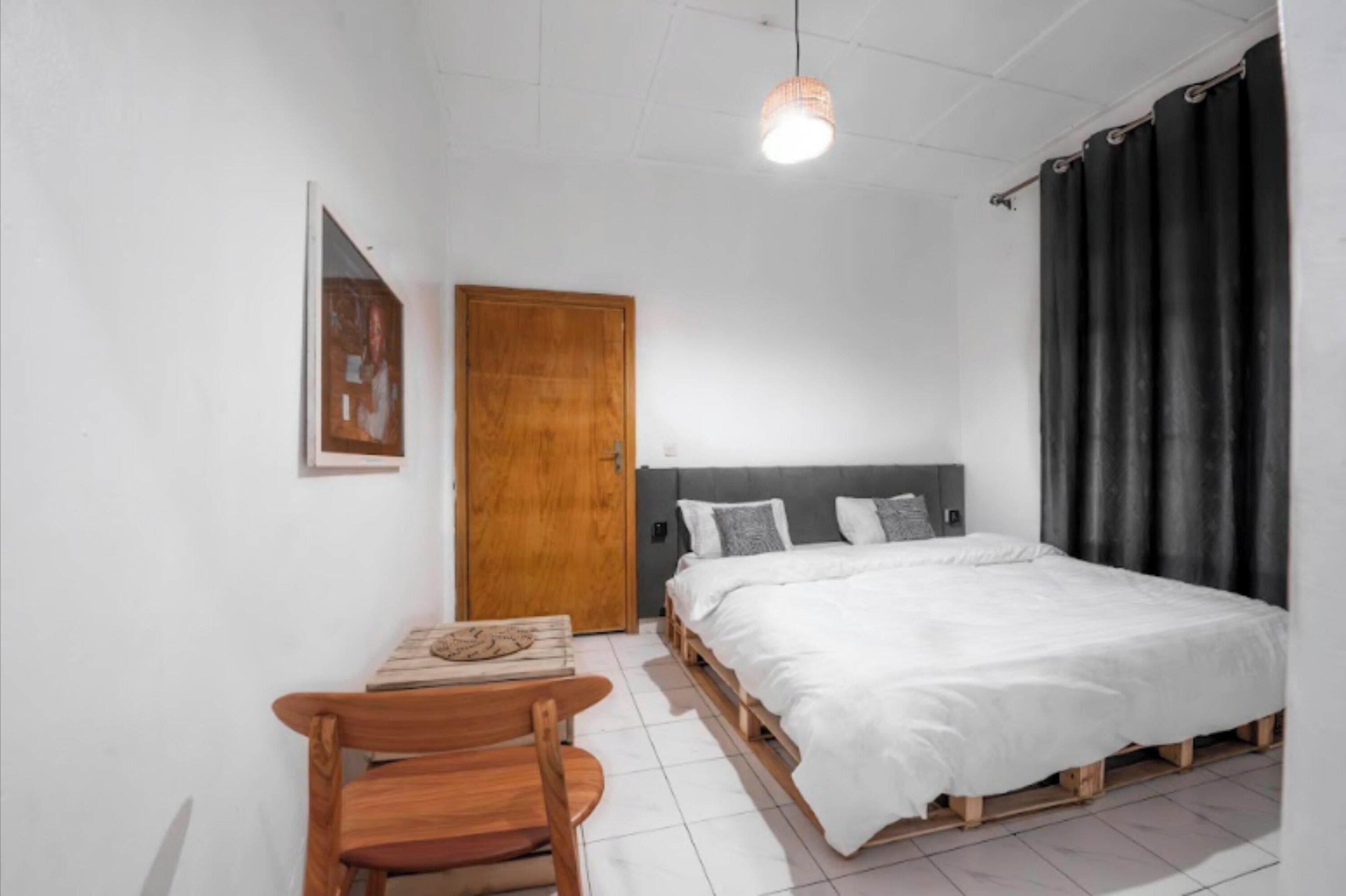 Une chambre à coucher avec un lit, une porte en bois, une petite table avec une chaise et un luminaire suspendu.