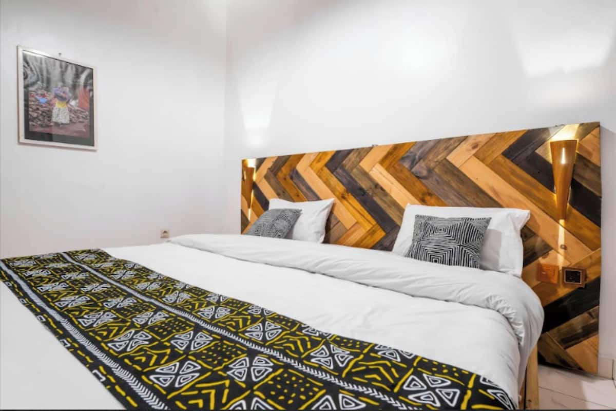 A bedroom with a herringbone-patterned headboard, a patterned bedspread, and a framed picture on the wall.