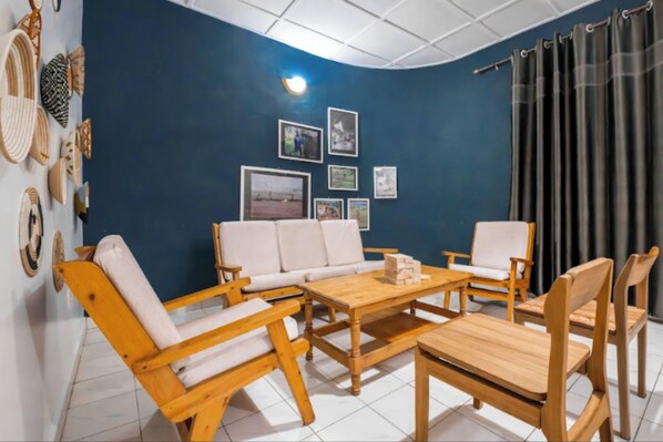A room with a blue accent wall, a white sofa, wooden chairs, a coffee table, and framed pictures. - Pili House & Garden Lodge Rwanda (Muhoza)