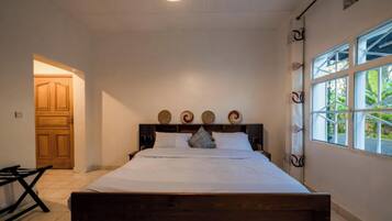 Un dormitorio con cama de madera, ventana con vista a la vegetación y puerta que da a otra habitación.