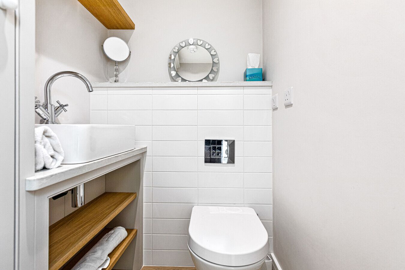 Een moderne badkamer met een witte wastafel, spiegel en toilet. Er is een handdoekhouder en een klein raam boven het toilet.
