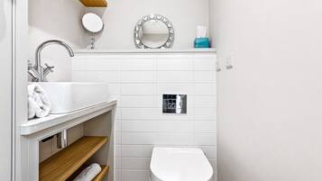 Een moderne badkamer met een witte wastafel, spiegel en toilet. Er is een handdoekhouder en een klein raam boven het toilet.