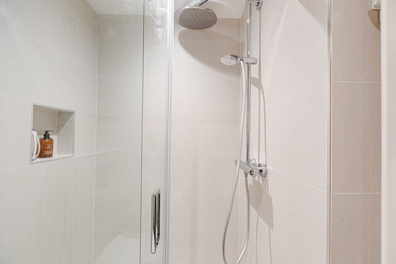 Una ducha moderna con un cabezal de ducha de mano y un cabezal de ducha de lluvia empotrado.