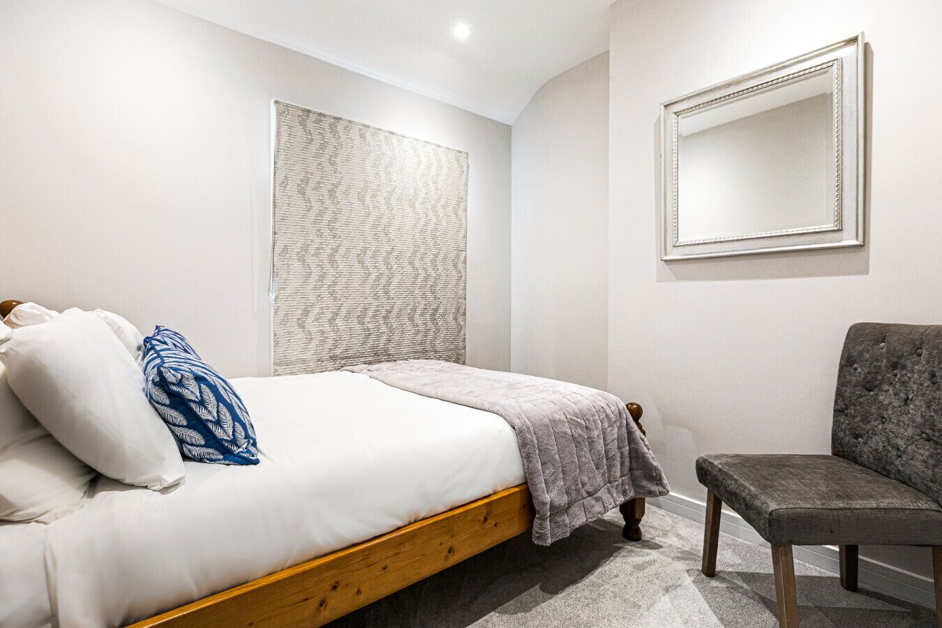 Een slaapkamer met een bed, een stoel, een grote spiegel en een gestructureerde wand.