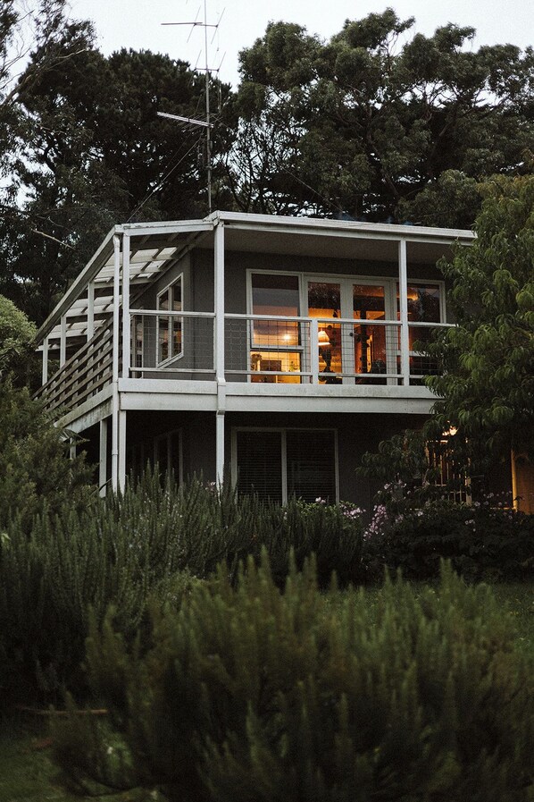 Une maison à deux étages dotée d’un balcon, entourée d’une végétation luxuriante.