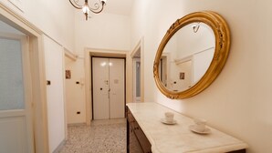 A hallway with a marble floor, a large mirror with a gold frame, and a small table with a cup and saucer.